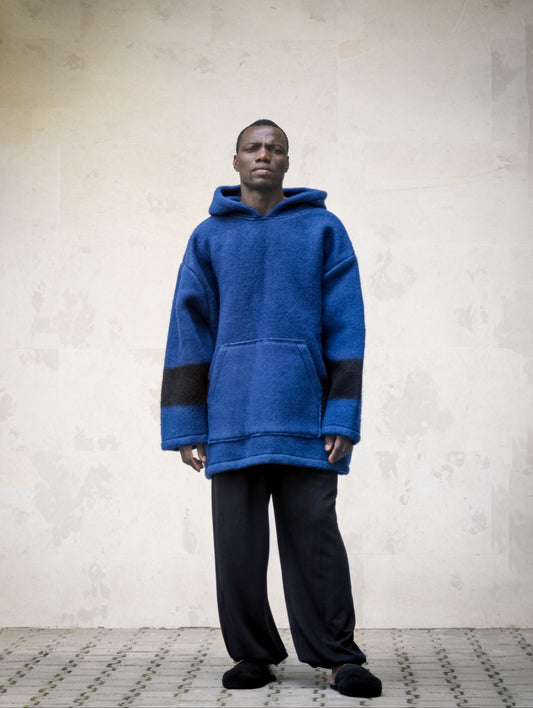 A man wearing a handwoven blue wool hoodie with black stripes and a big front pocket.