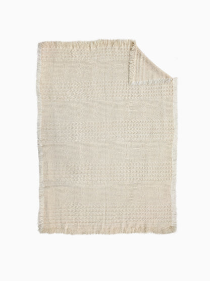 An organic wool blanket in natural ight beige or cream color, featuring a textured basketweave pattern and fringed edges.