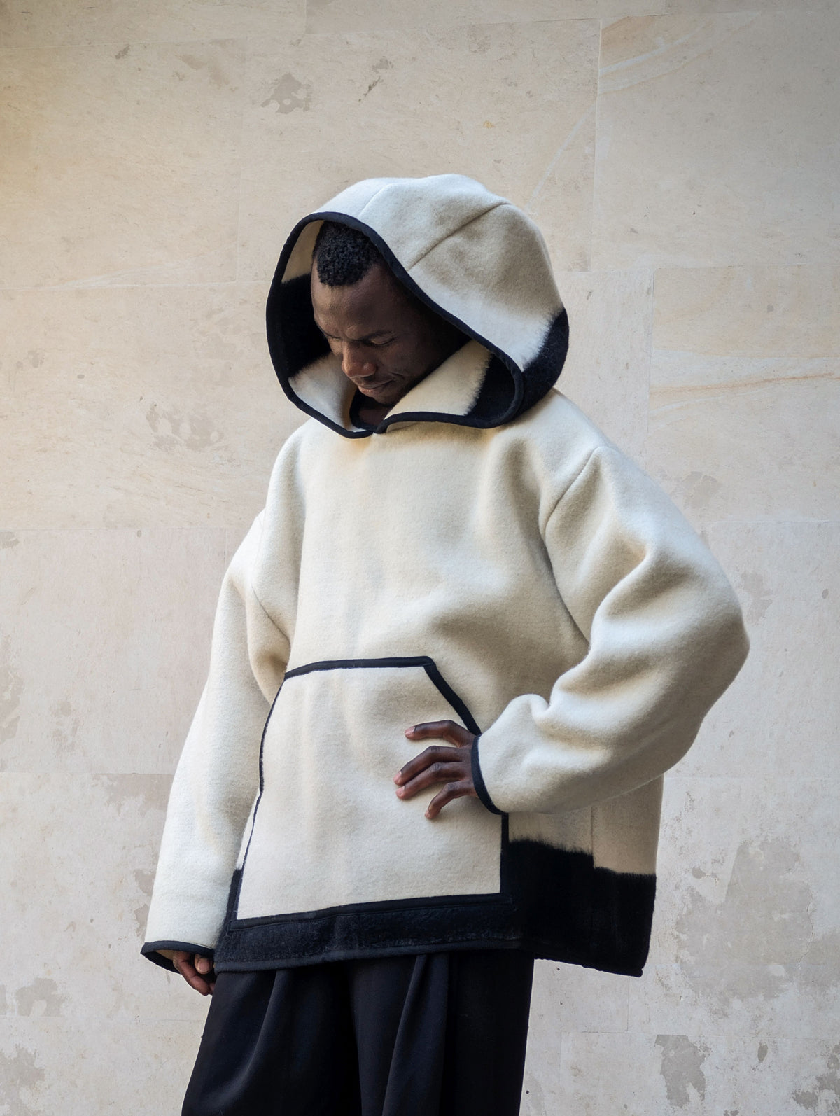 A person wearing an ivory-colored hooded jacket or anorak tailored from avirgin wool blanket.