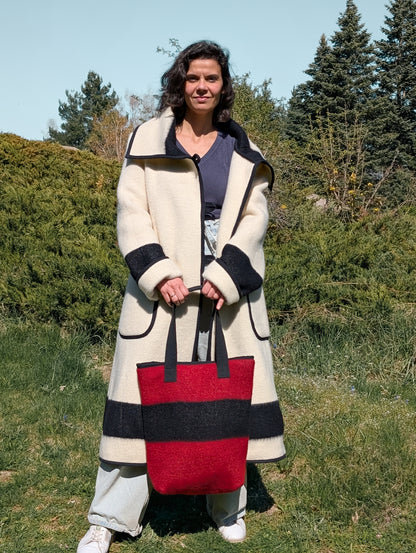 Woman wearing a long cream overcoat and a red bag in the same style, both made from repurposed handwoven wool blankets.