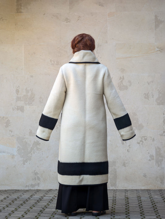 Back view of women's off-white handwoven wool coat with wide collar, black stripe hem and long tailored silhouette