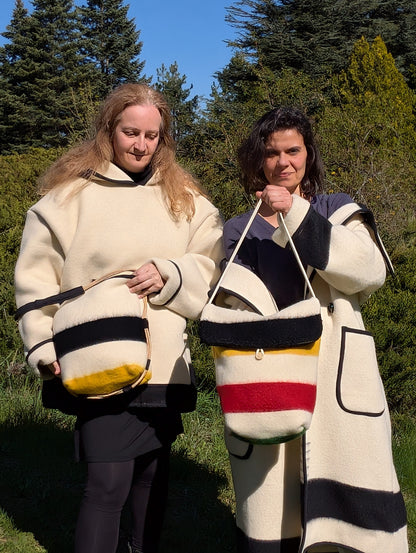 Two people wearing patterned cloaks holding stylish wool blanket bags. 