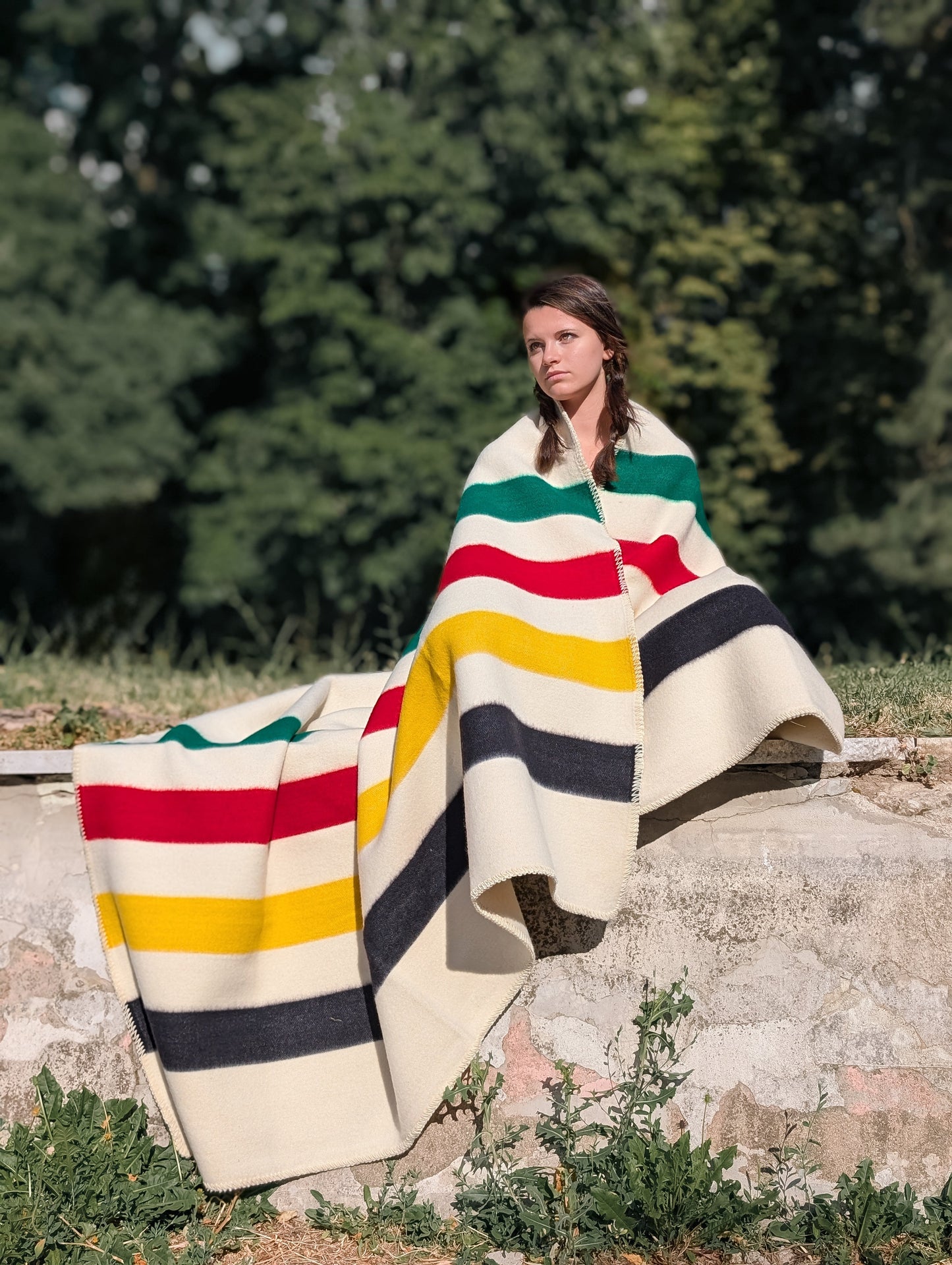 A sitting woman wrapped in a thick traditional off-white wool throw with iconic stripes pattern