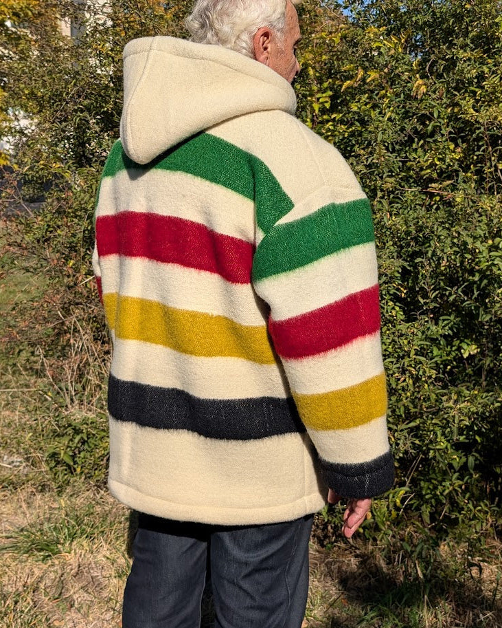 An elderly man wearing a pure wool multistriped anorak with a big front kangaroo pocket, unisex boreal shirt, camp sweater upcycled from sustainable eco wool blanket 
