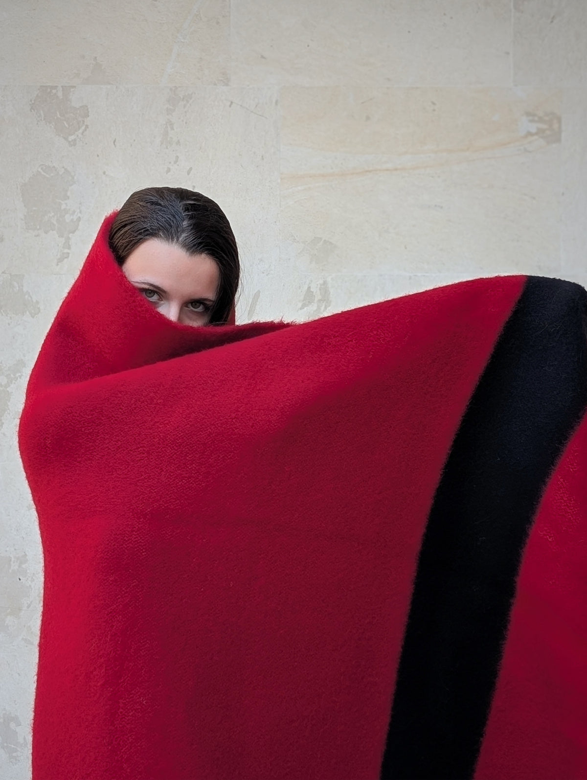 Woman wrapped in a large luxurious red wool blanket with a solid black stripe.