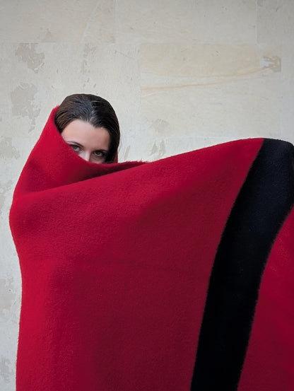 Woman wrapped in a large luxurious red wool blanket with a solid black stripe.