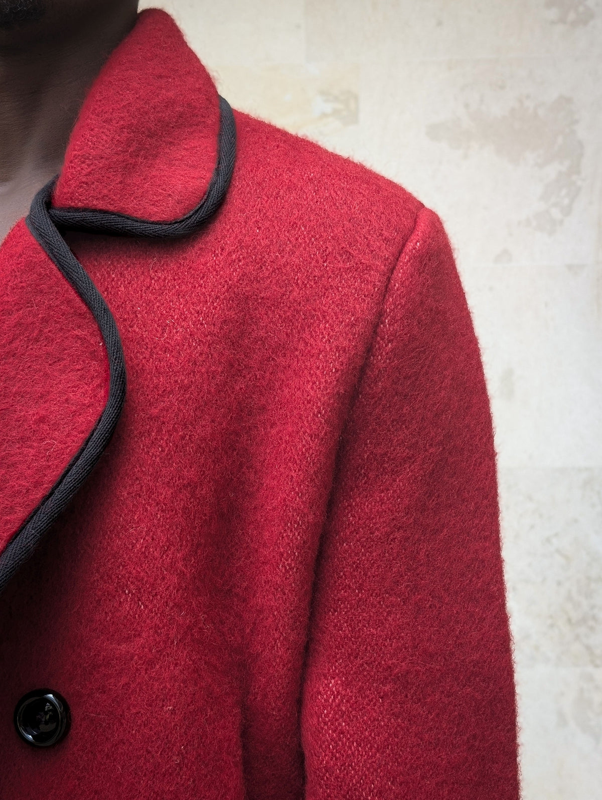 Close-up shot of handwoven red virgin wool fabric cut from an original handwoven blanket, detailing the black bound edge piping and wide collar of a classic blanket jacket.