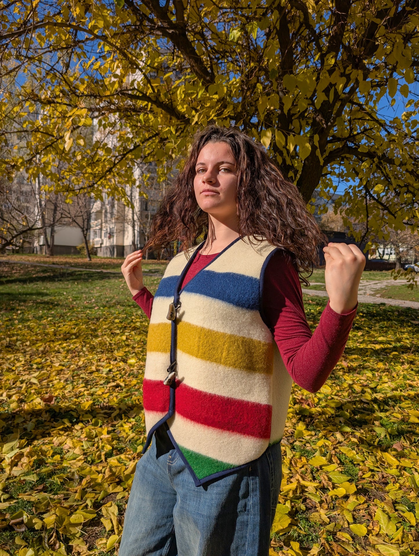 A young woman wearing a gorgeous vest cut from a new handwoven wool blanket, with multicolor stripes and off-white base color. Great for any ocassion.