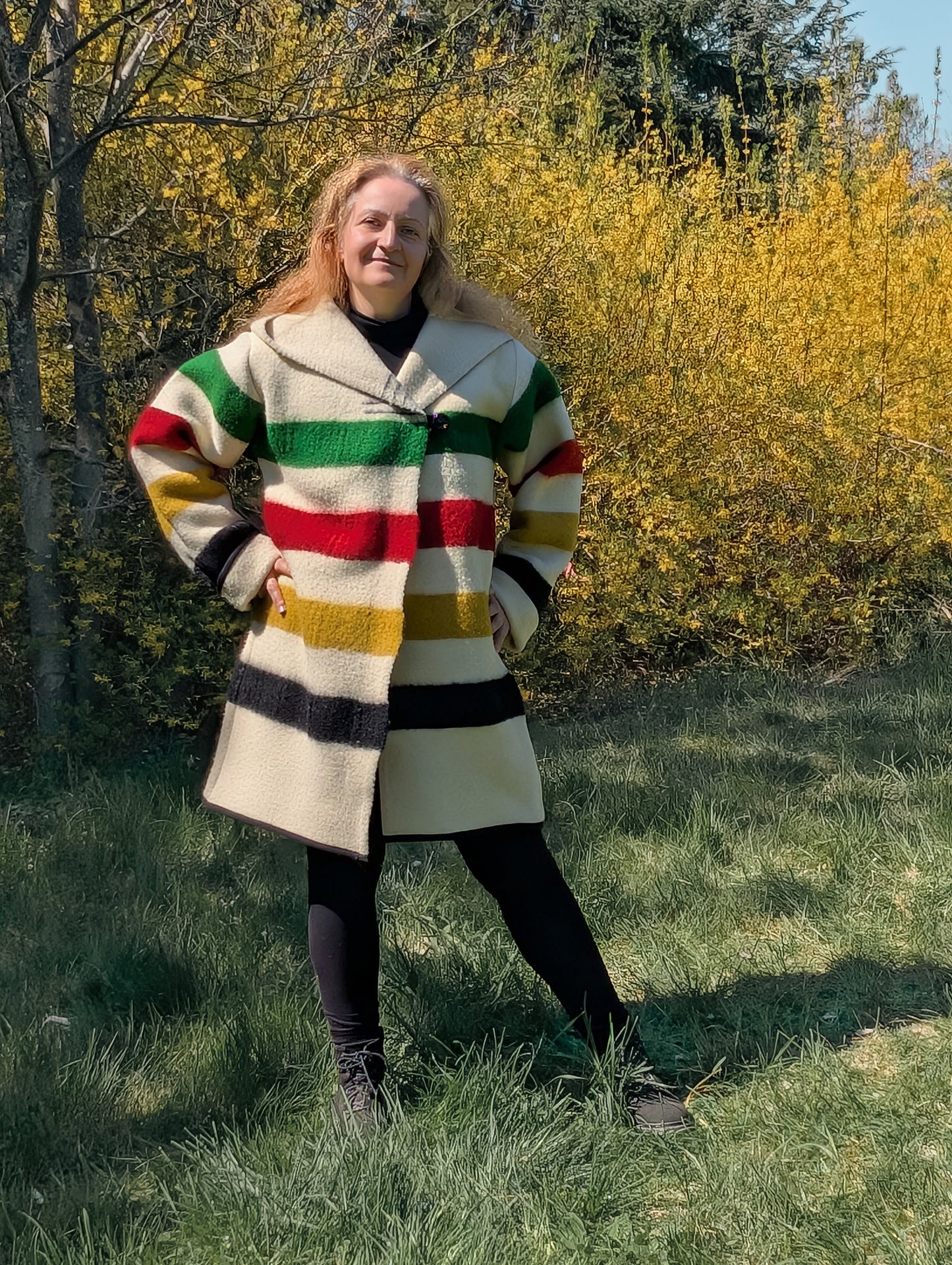A woman posing with a thick loose swing capote coat in midi size handmade from a multistriped  blanket. 