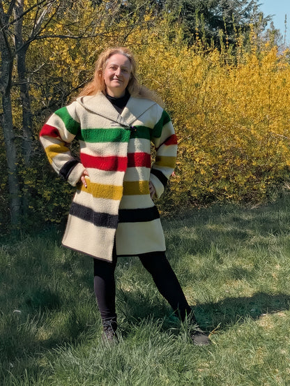 A woman posing with a thick loose swing capote coat in midi size handmade from a multistriped  blanket. 