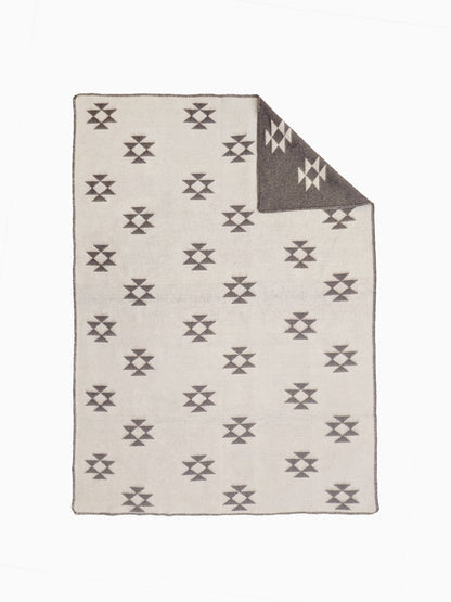 An undyed wool blanket throw with a light beige base and repeating earth brown geometric aztec pattern, shown with one corner folded over to reveal the reverse side.