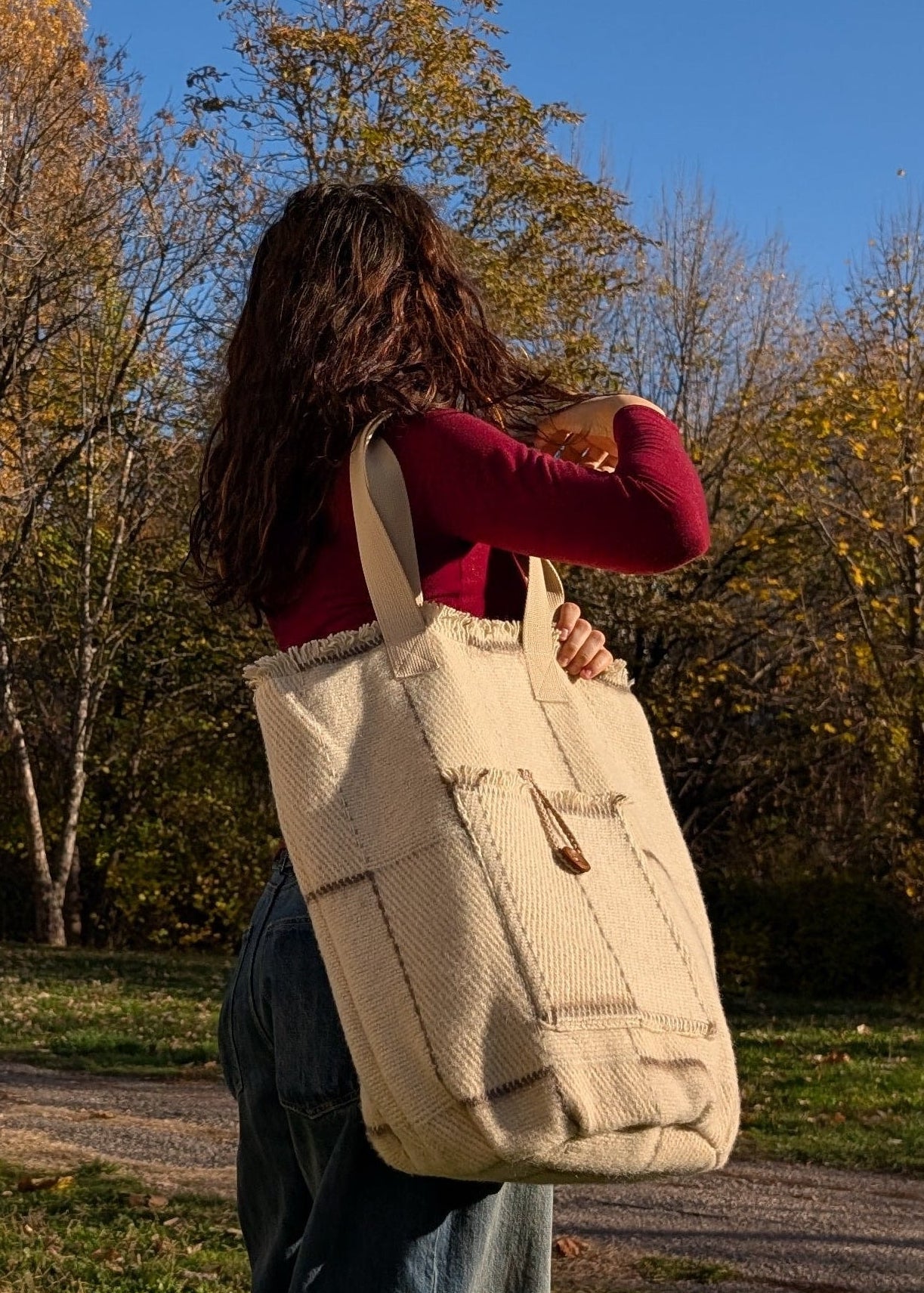 Woman wearing a large unisex blanket tote or market bag with minimalistic geometric patterns and soft earth tones.