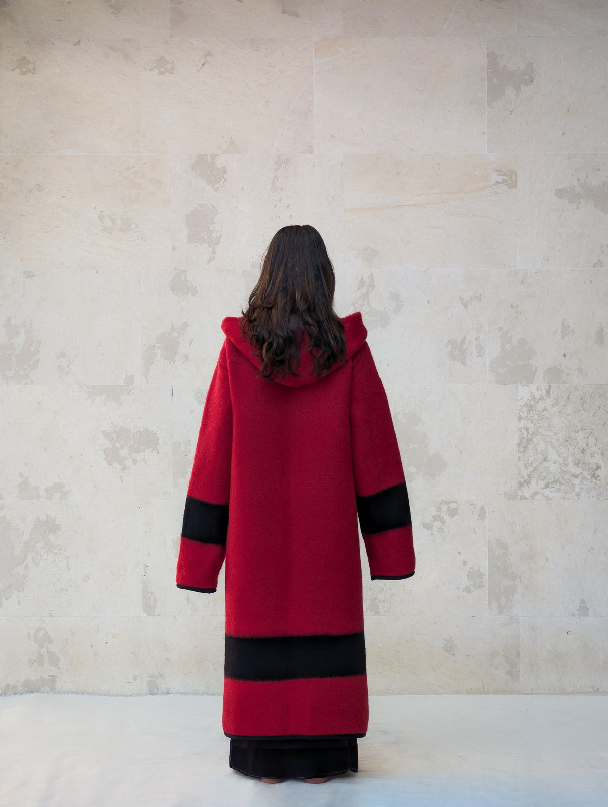 Back view of women's red hooded wool coat with black stripe sleeves and hem in handwoven wool