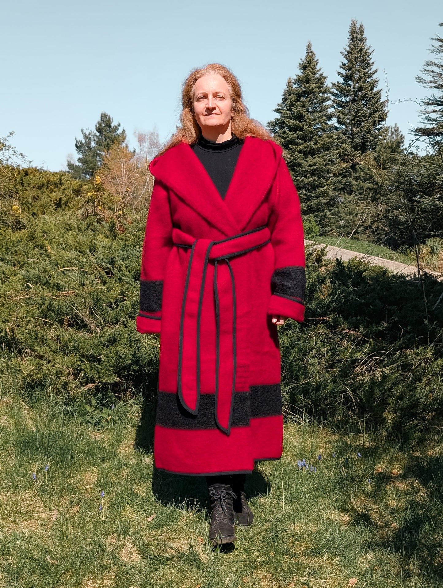 A woman posing with a luxurious bespoke capote coat, wrapped with a belt, with a wide hood and a belt.