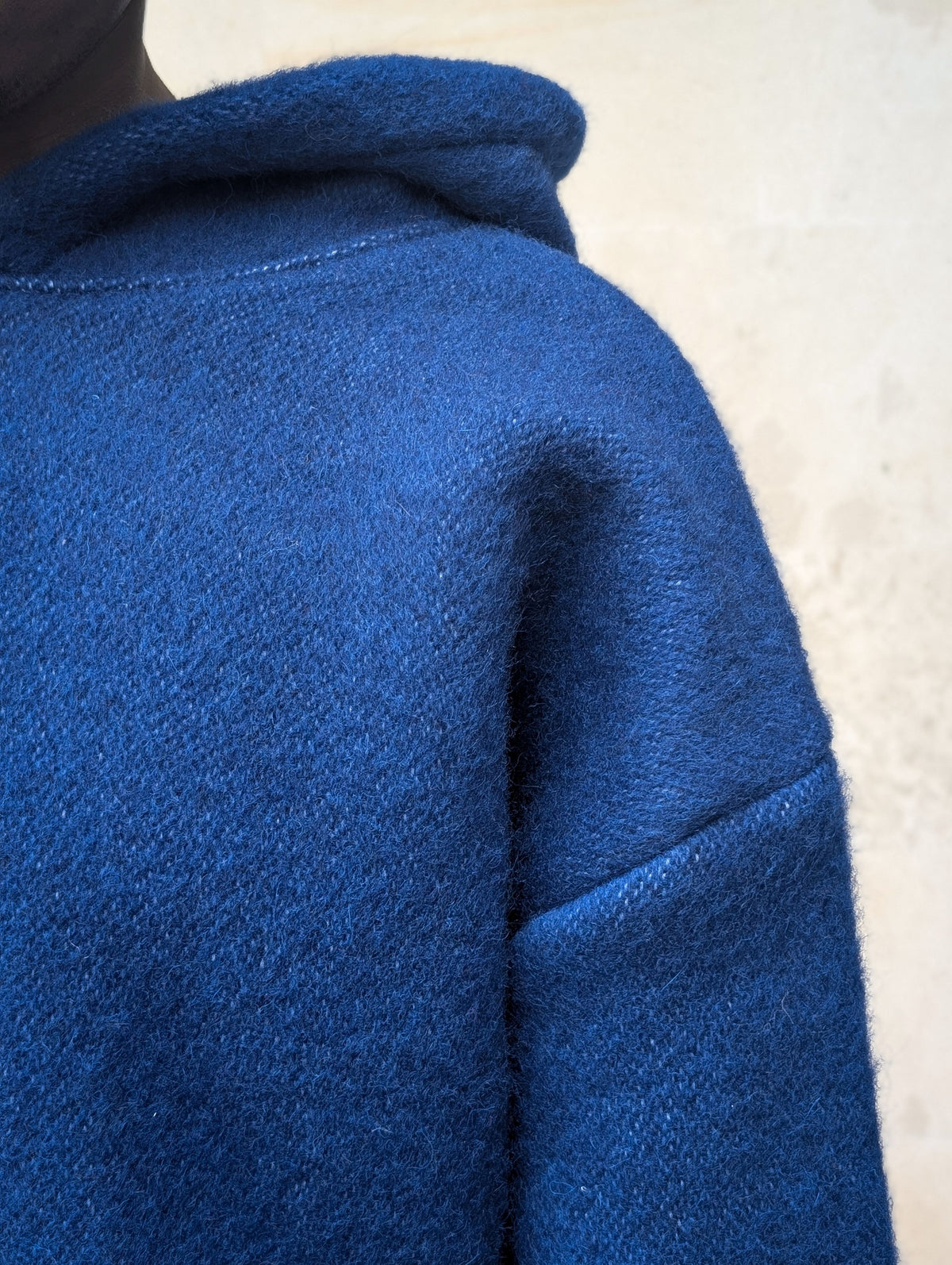 Close-up texture detail of handwoven blue pure virgin wool fabric on a blanket hoodie shoulder.