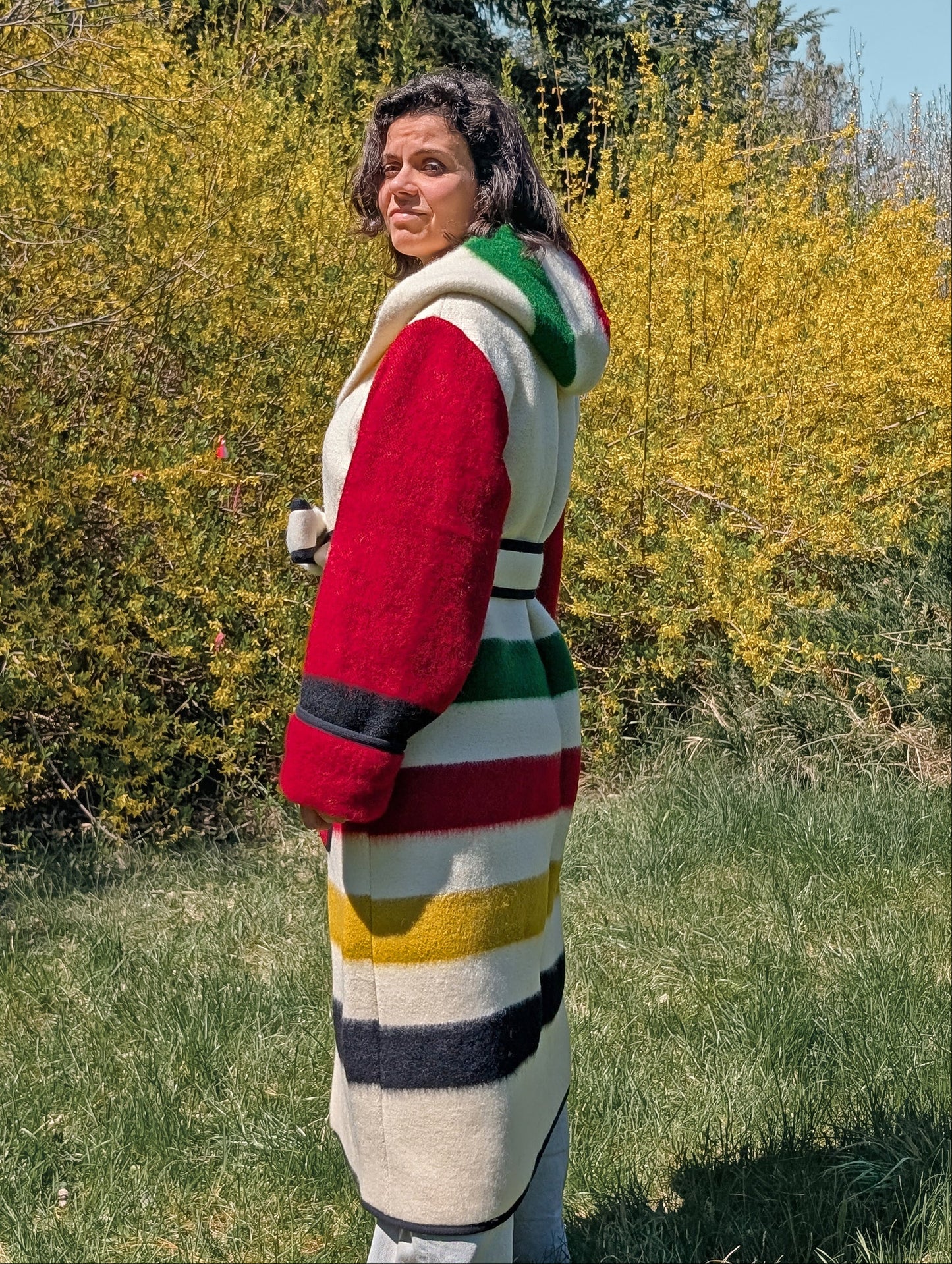 Woman posing with a cozy warm unisex blanket overcoat, made of iconic traditional handwoven stripe wool blanket.