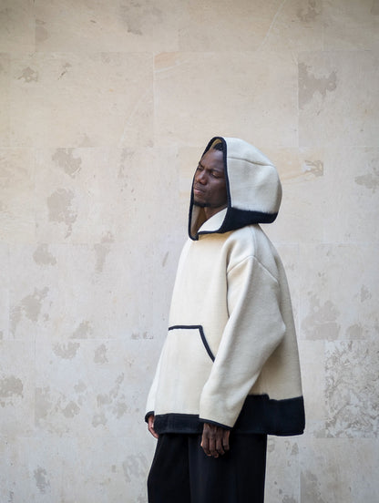 A model wearing a cream-colored hooded anorak made from handmade pure virgin wool blanket.