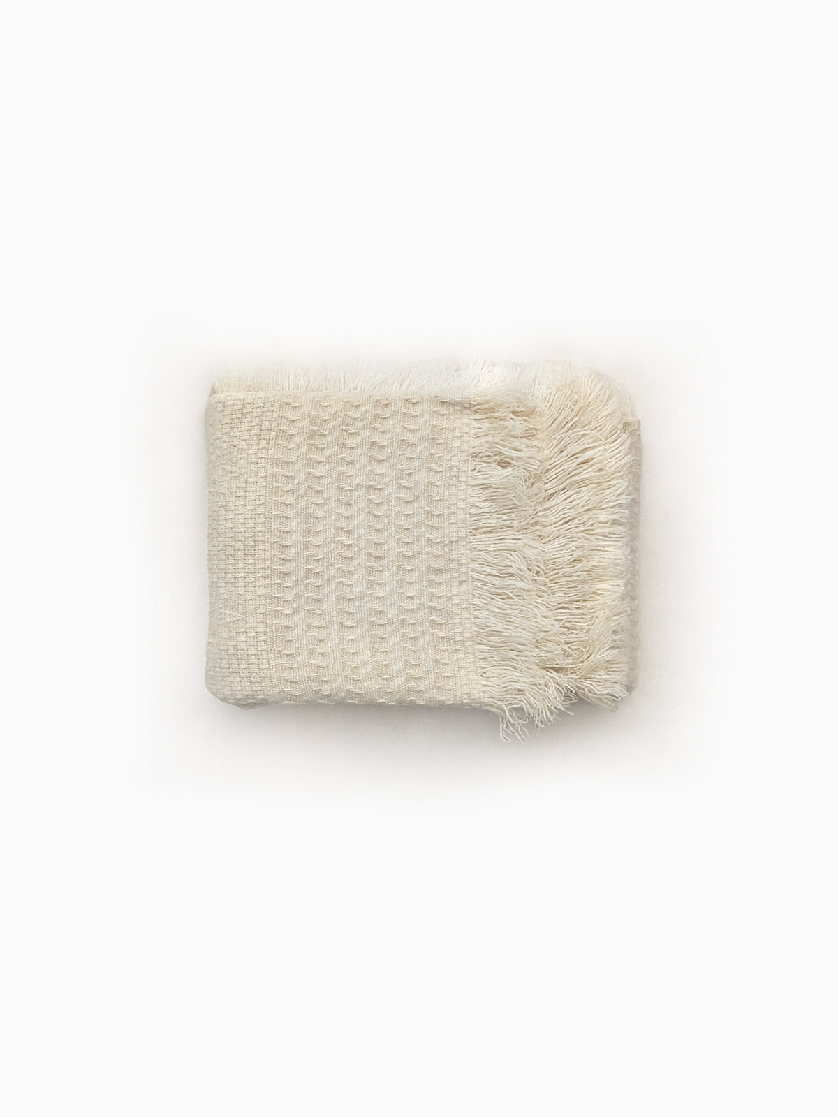 A folded natural cream-colored handwoven blanket with textured weave and fringed edges.