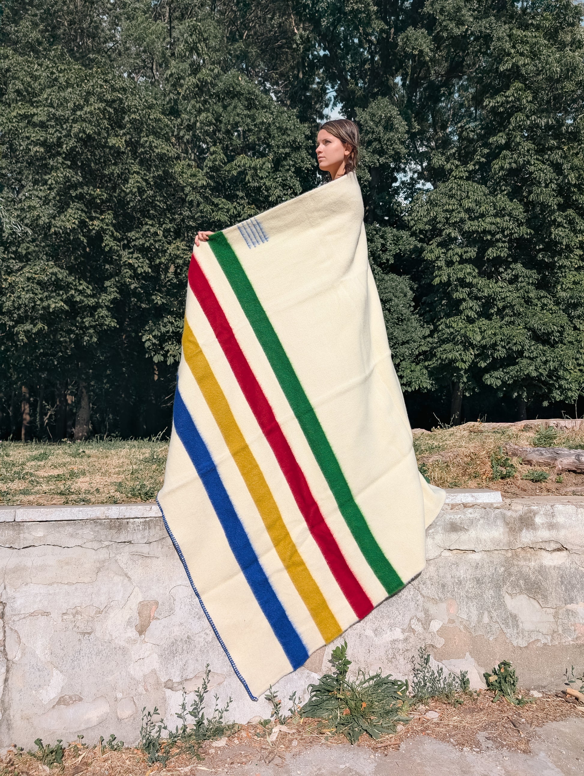 A girl holding a multistripe wool blanket in cream with multicolor stripes in a park