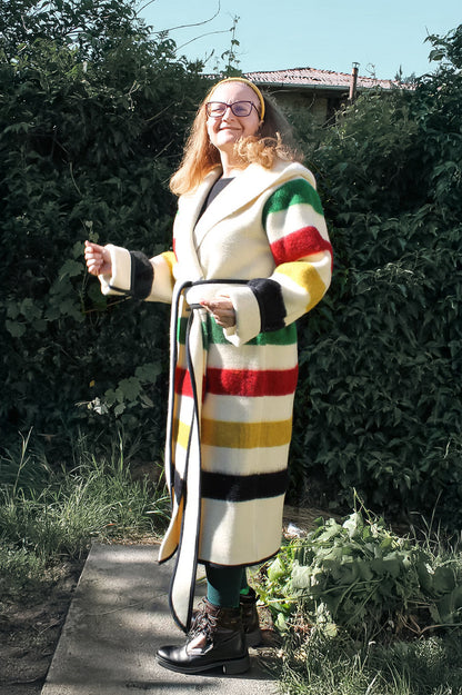 Woman wearing a colorful striped metis capote coat standing outdoors. The coat is handmade from sustainable eco wool  blanket.