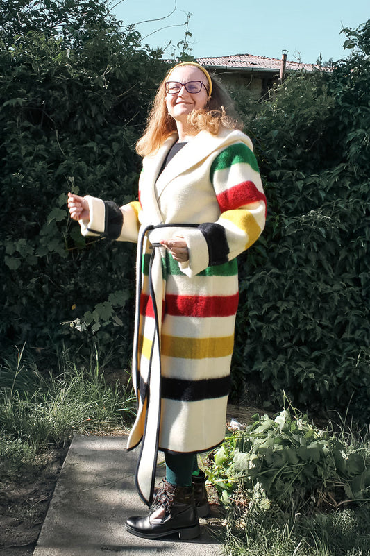 Woman wearing a colorful striped metis capote coat standing outdoors. The coat is handmade from sustainable eco wool  blanket.