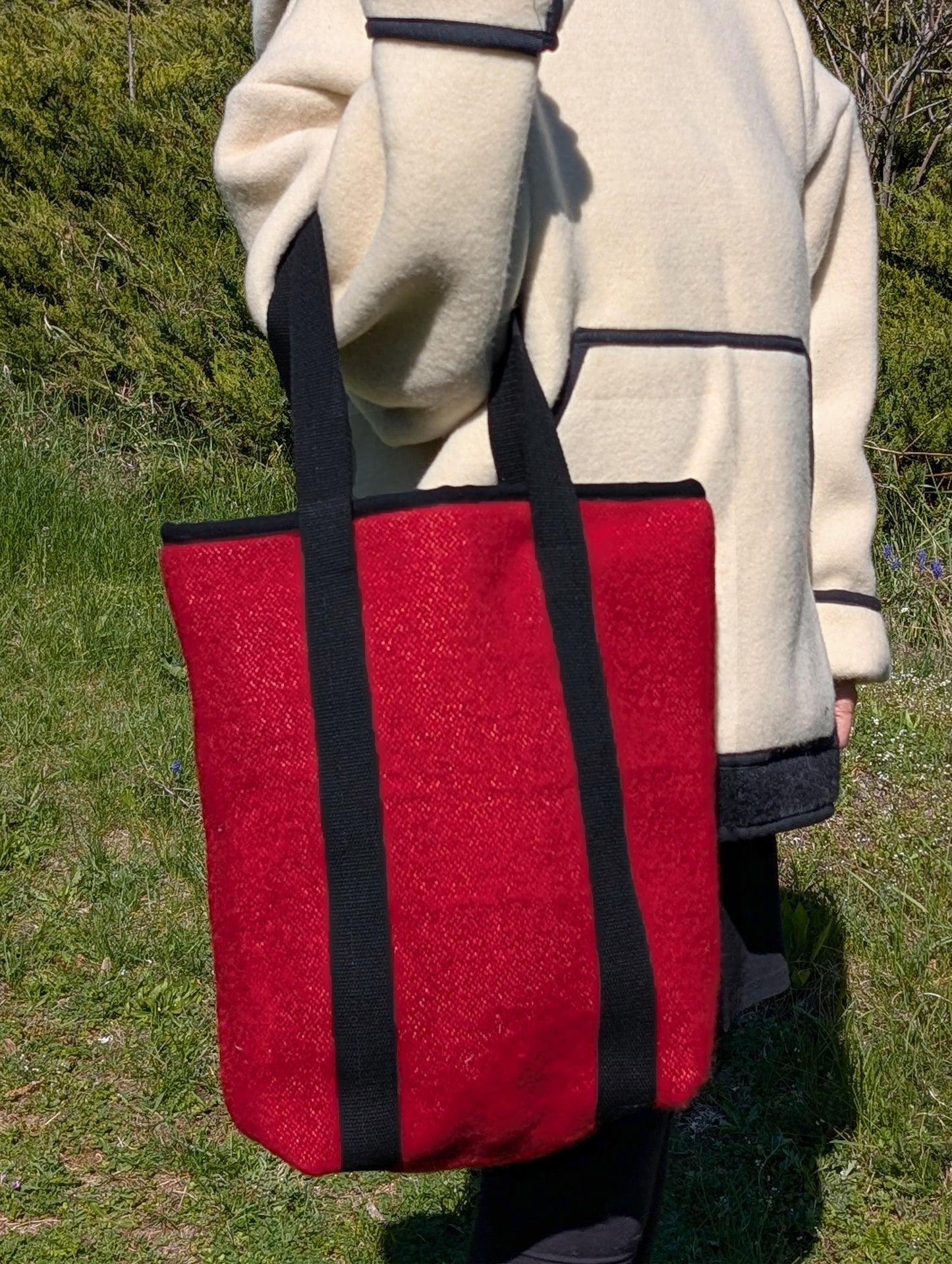 Woman holding a bold red tote bag with black vertical straps. A bespoke shopping bag upcycled from original authentic handwoven blanket in a small family studio.