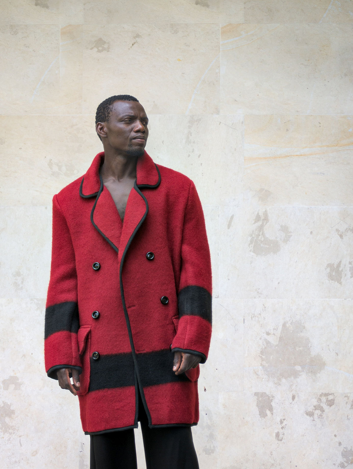 A front view of a model in a tailored red wool peacoat showing black double-breasted buttons and black stripe details.