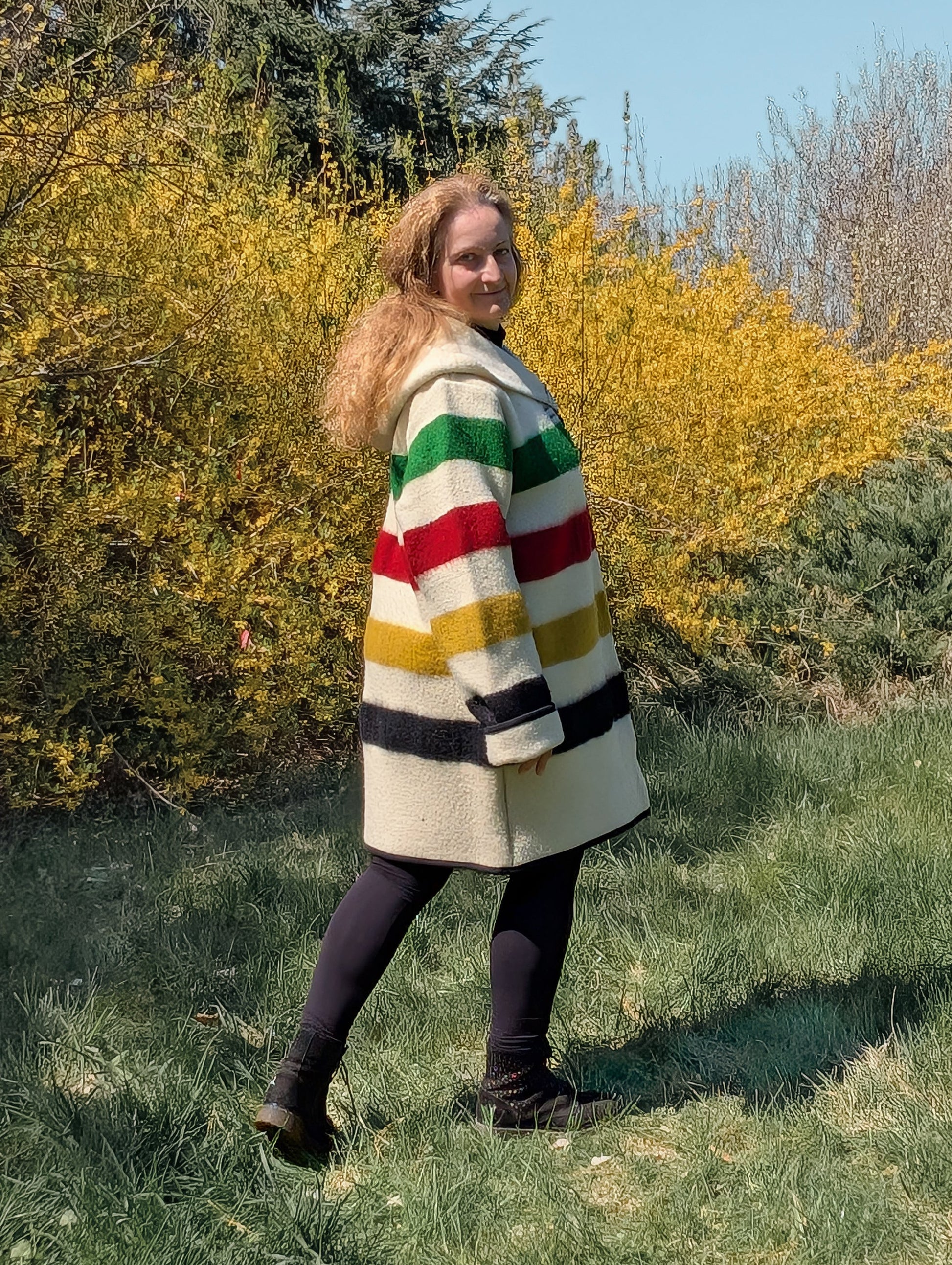 A woman posing with a thick loose midi swing coat with shawl collar and wide hoodie  handmade from a traditional stripe blanket. 