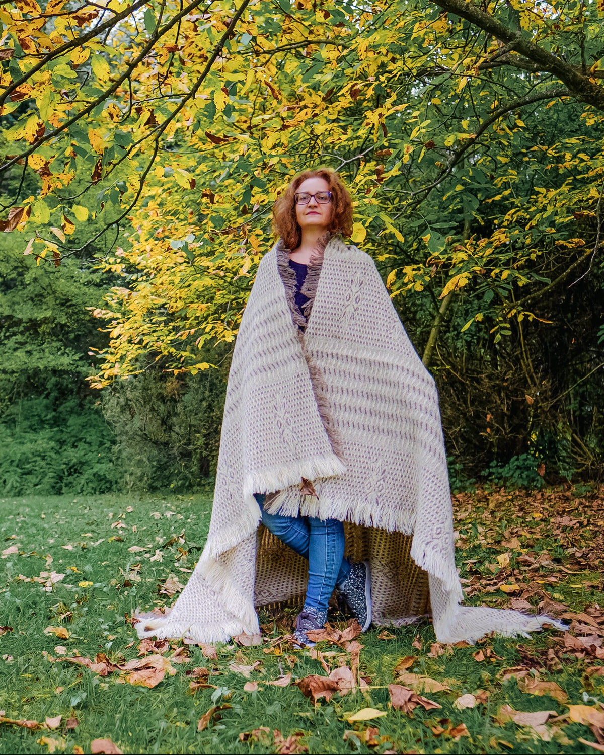 Woman wrapped in a handwoven undyed wool throw, taupe and cream structured weave, worn outdoors in autumn