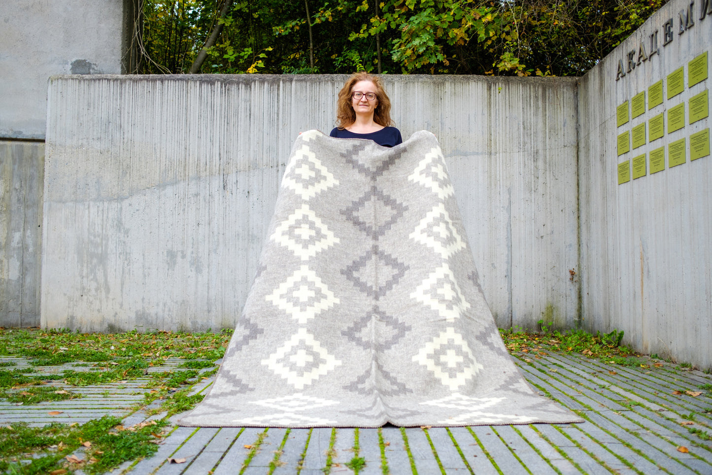 Woman standing outdoors with a large undyed gray and white patterned blanket draped over her. The blanket is handmade from premium quality new pure wool.