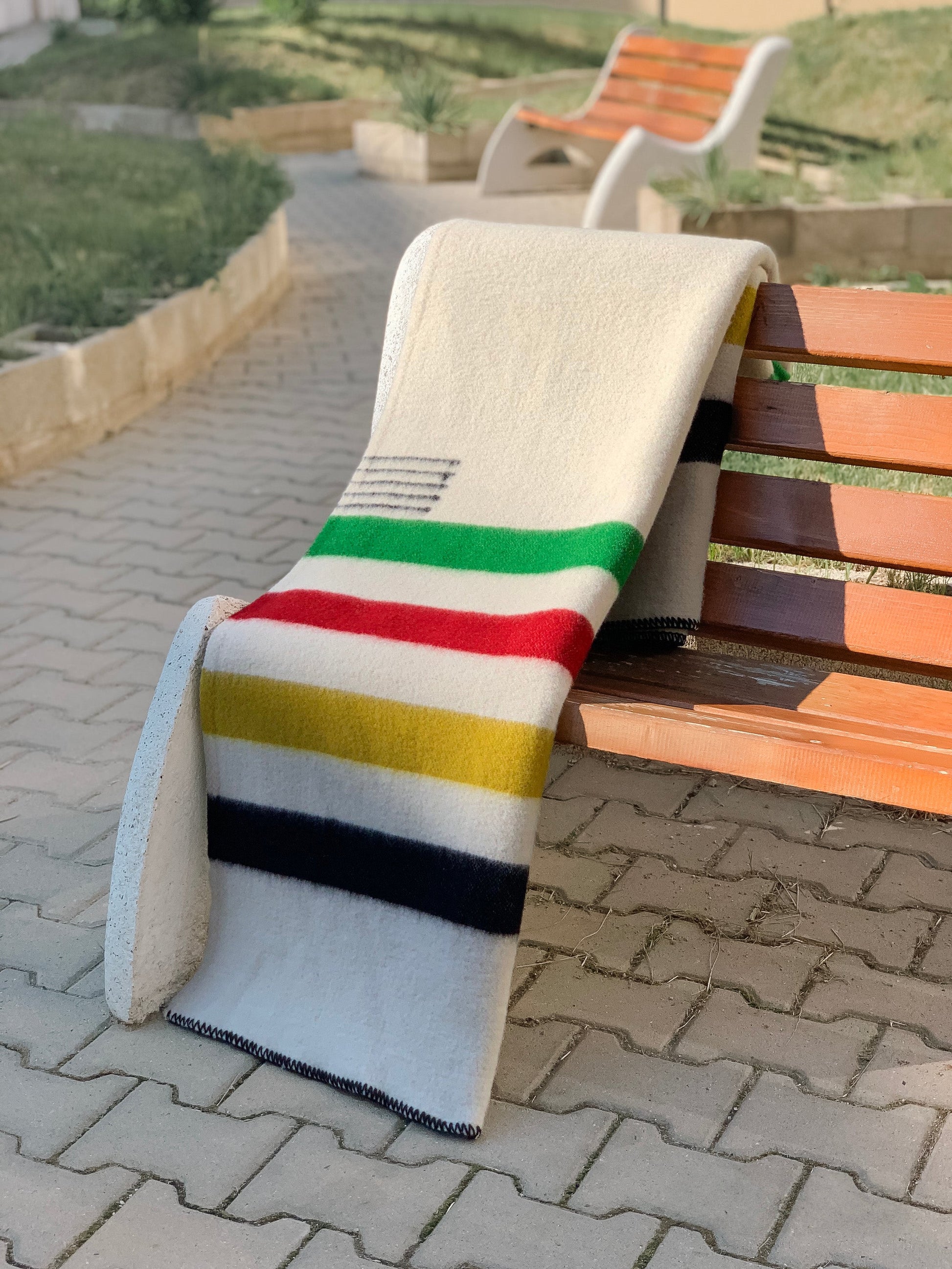 A thick warm heritage multistripe wool  blanket in cream on a bench