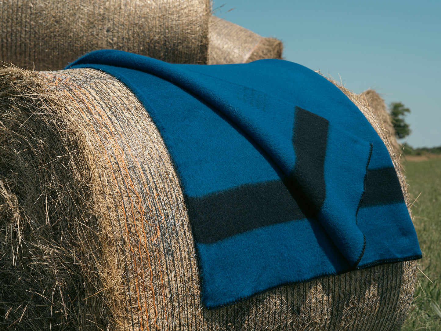 Blue hygge wool blanket draped over a hay bale with a clear sky background