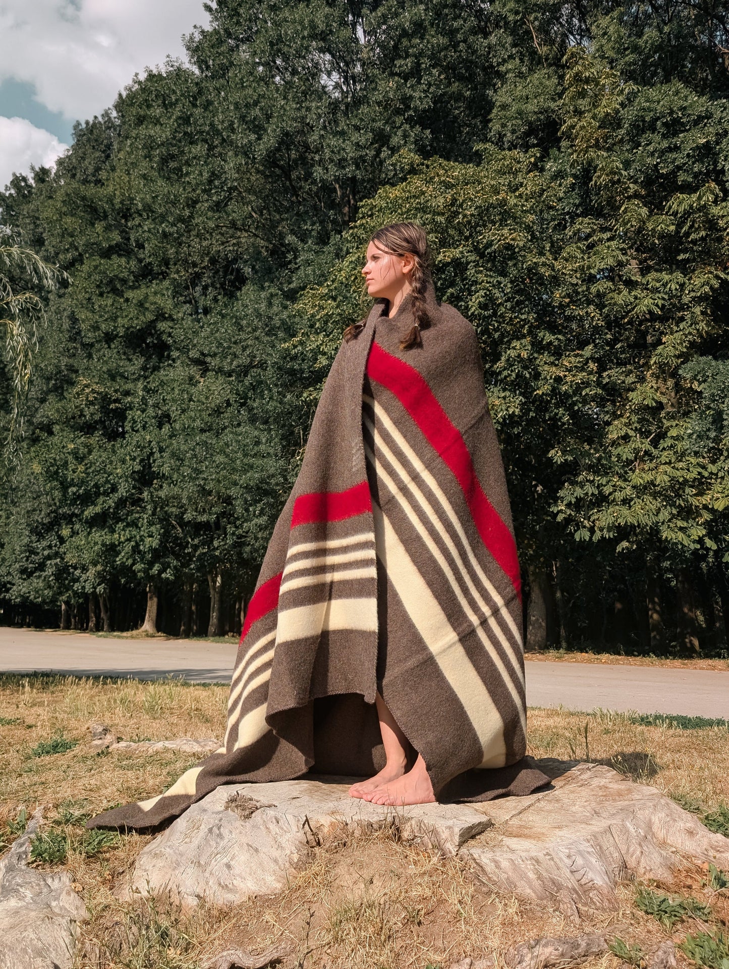 A standing girl wrapped in a heritage brown blanket with red and white  stripes