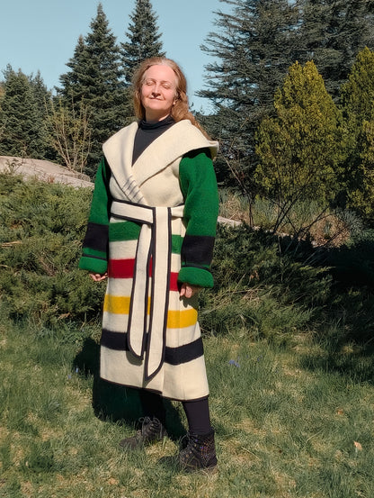 A woman posing with a wrap capote coat with a large hood, cinched with a belt. Made from repurposed stripe wool blanket.