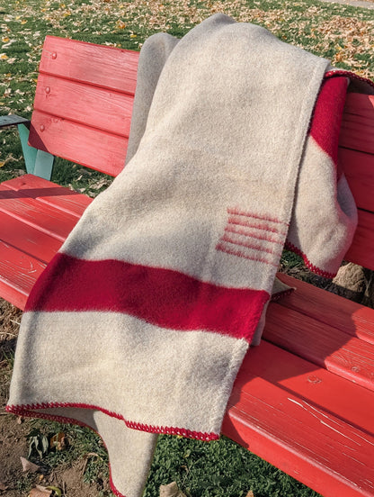 Heavy natural organic gray wool blanket with red stripes, draped on a red bench outside in a park.
