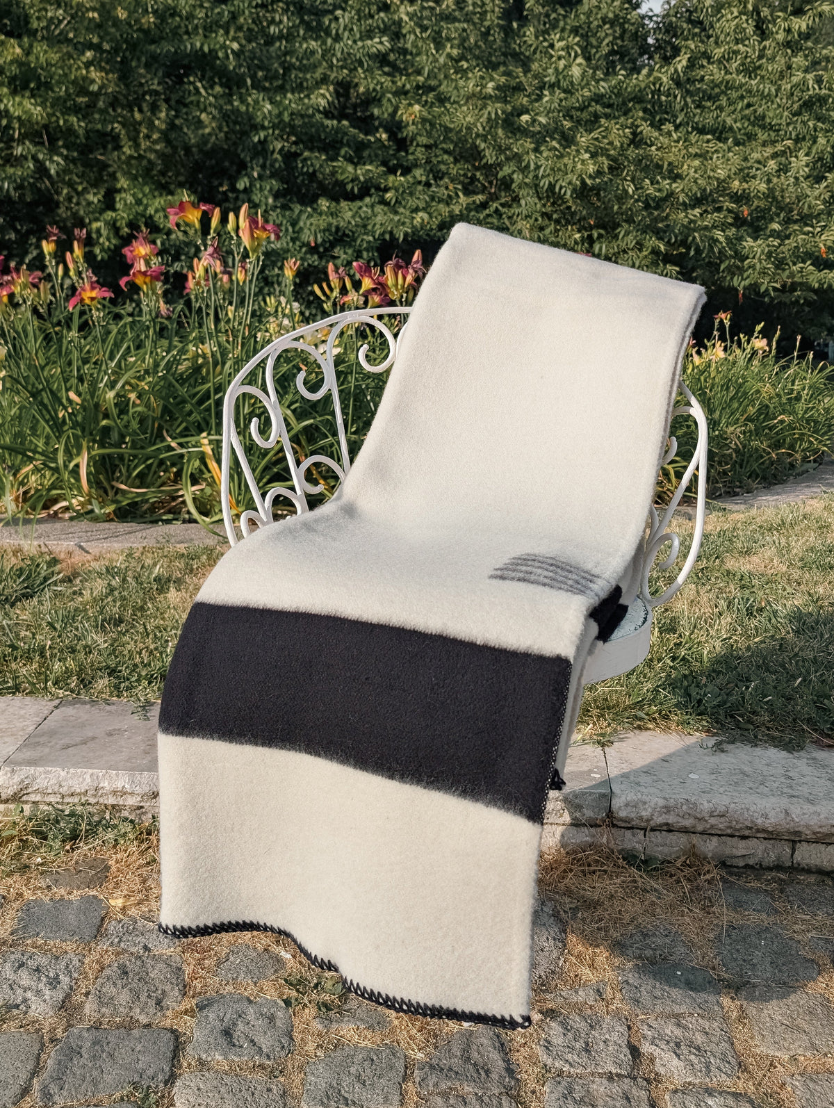 Cream wool blanket with black stripes set on white lounge chair out in the park. Great for luxurious gift for home and decor.