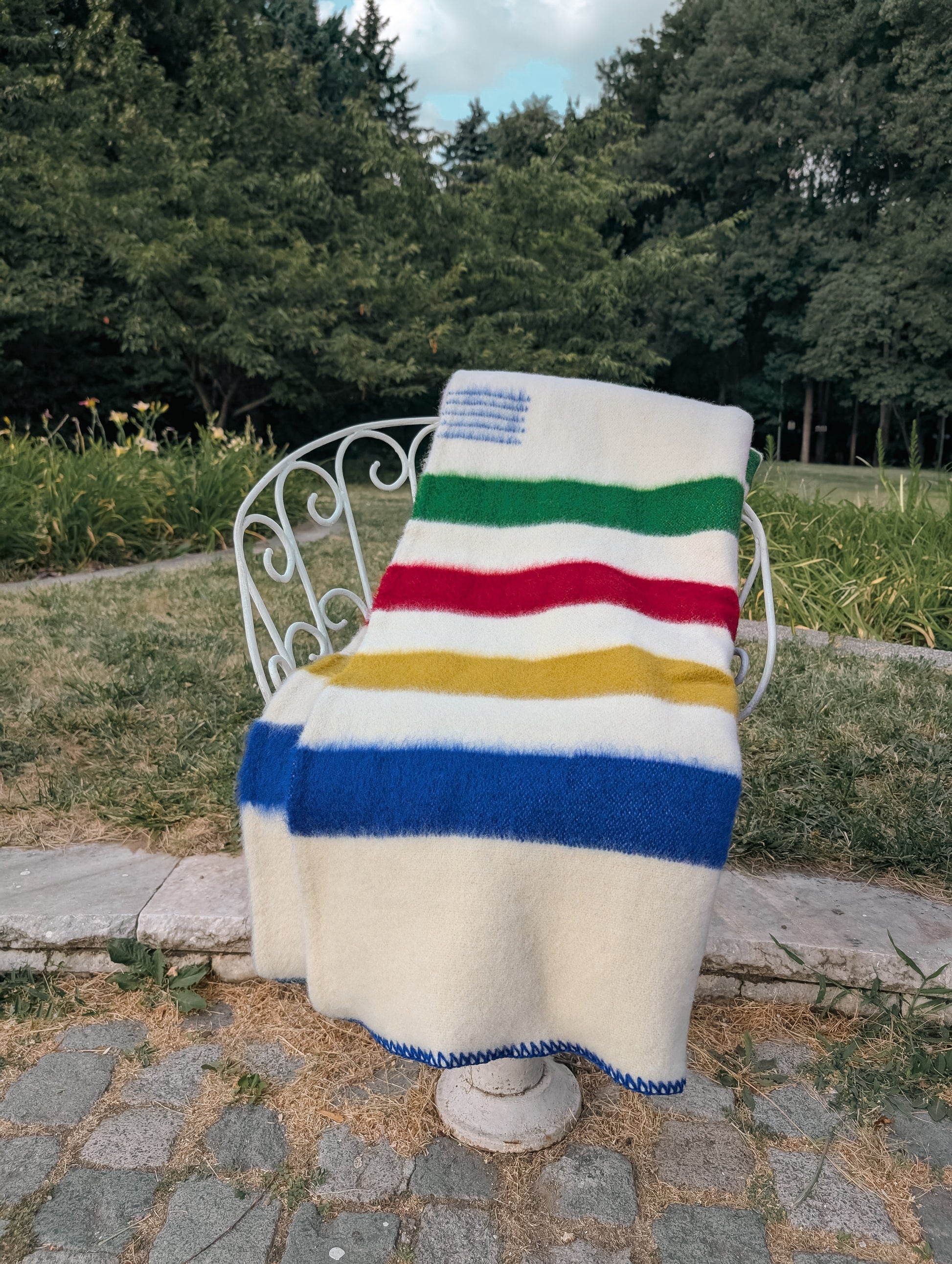 multistripe wool blanket draped over a chair outdoors with trees in the background