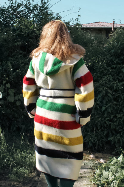 A woman wearing a multistriped wool metis capote coat with wide hoodie and a belt, upcycled from a virgin wool  blanket.