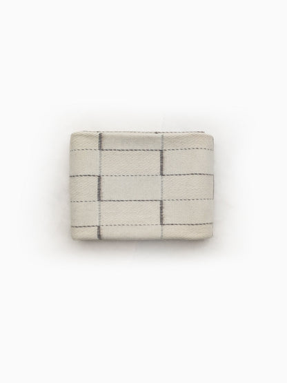 Folded undyed handwoven wool blanket in natural ivory/cream or offwhite with geometric grid weave detail.