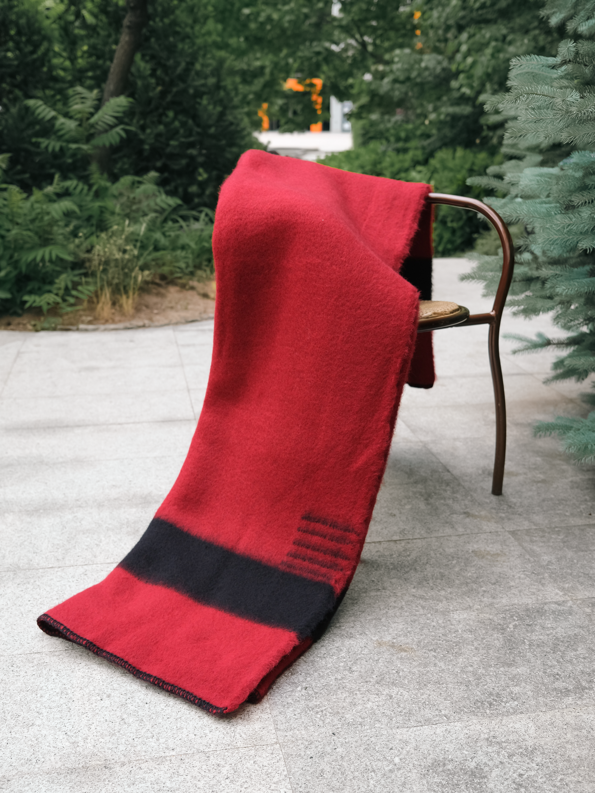 A handmade Frontier inspired rustic winter wool throw in red with a black stripe, draped on a chair.