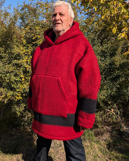 Man wearing a red hooded coat or also woolen hoodie standing outdoors with trees in the background.