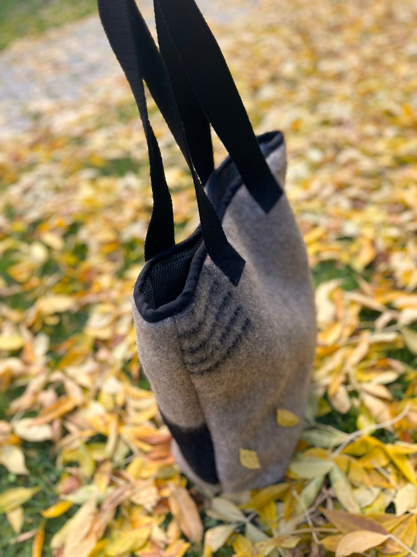 Upcycled gray blanket stripe bag on a ground covered with yellow leaves.