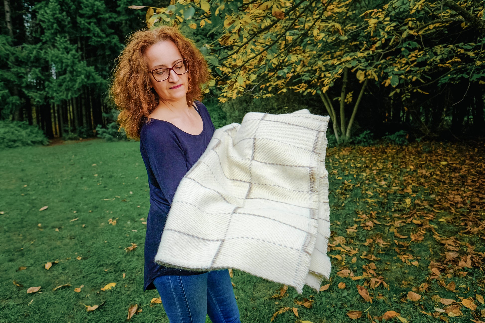 Woman holding a white woven blanket made of undyed virgin wool outdoors in a garden setting.