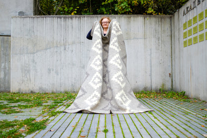 Person holding a large thick woolen blanket with ancient aztec diamond pattern. Warm, cozy and beautiful, ideal for modern minimalistic interior. 