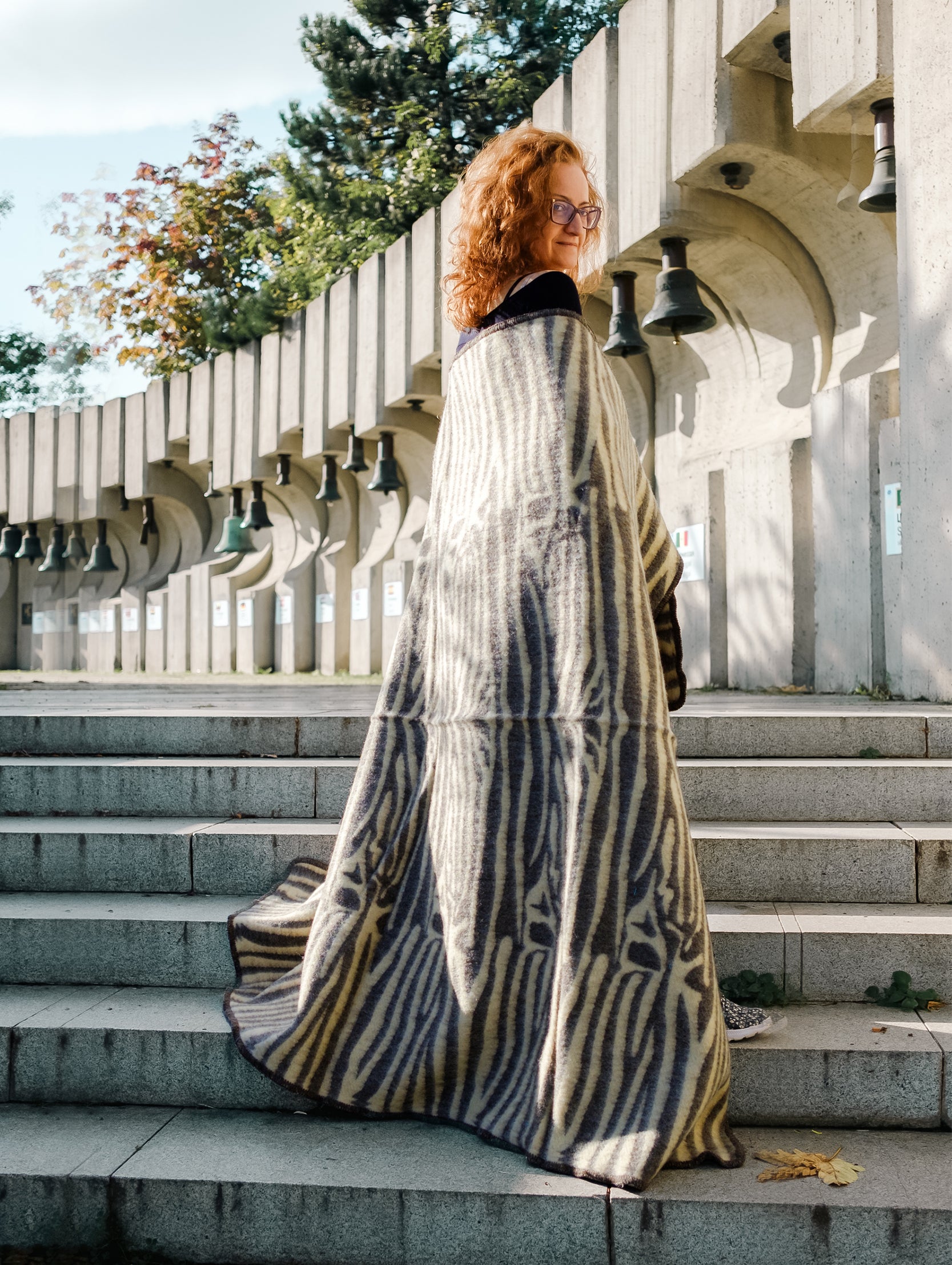 Person wearing a patterned undyed wool throw, standing on steps outdoors. This blanket is soft, warm and great for home decor