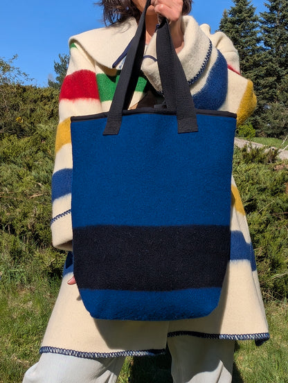 Person holding a blue tote bag with black stripe made from iconic heritage blanket