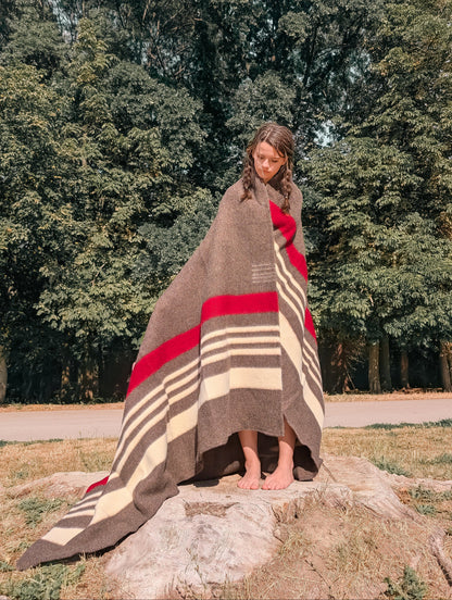 A girl standing in an outdoor natural setting and wearing a heirloom rustic brown stripe cabin throw handwoven from 100% pure sheep wool