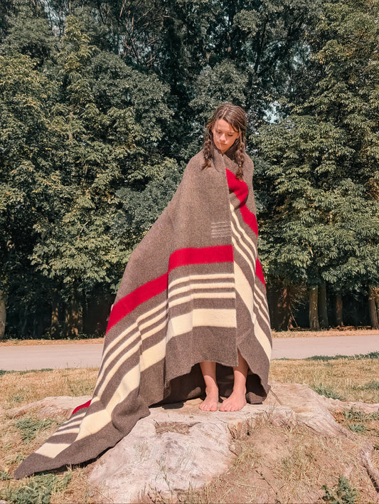 A girl standing in an outdoor natural setting and wearing a heirloom rustic brown stripe cabin throw handwoven from 100% pure sheep wool