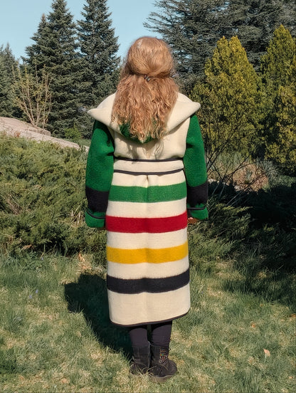 A woman wearing a statement blanket capote coat with iconic stripes and a hood. 