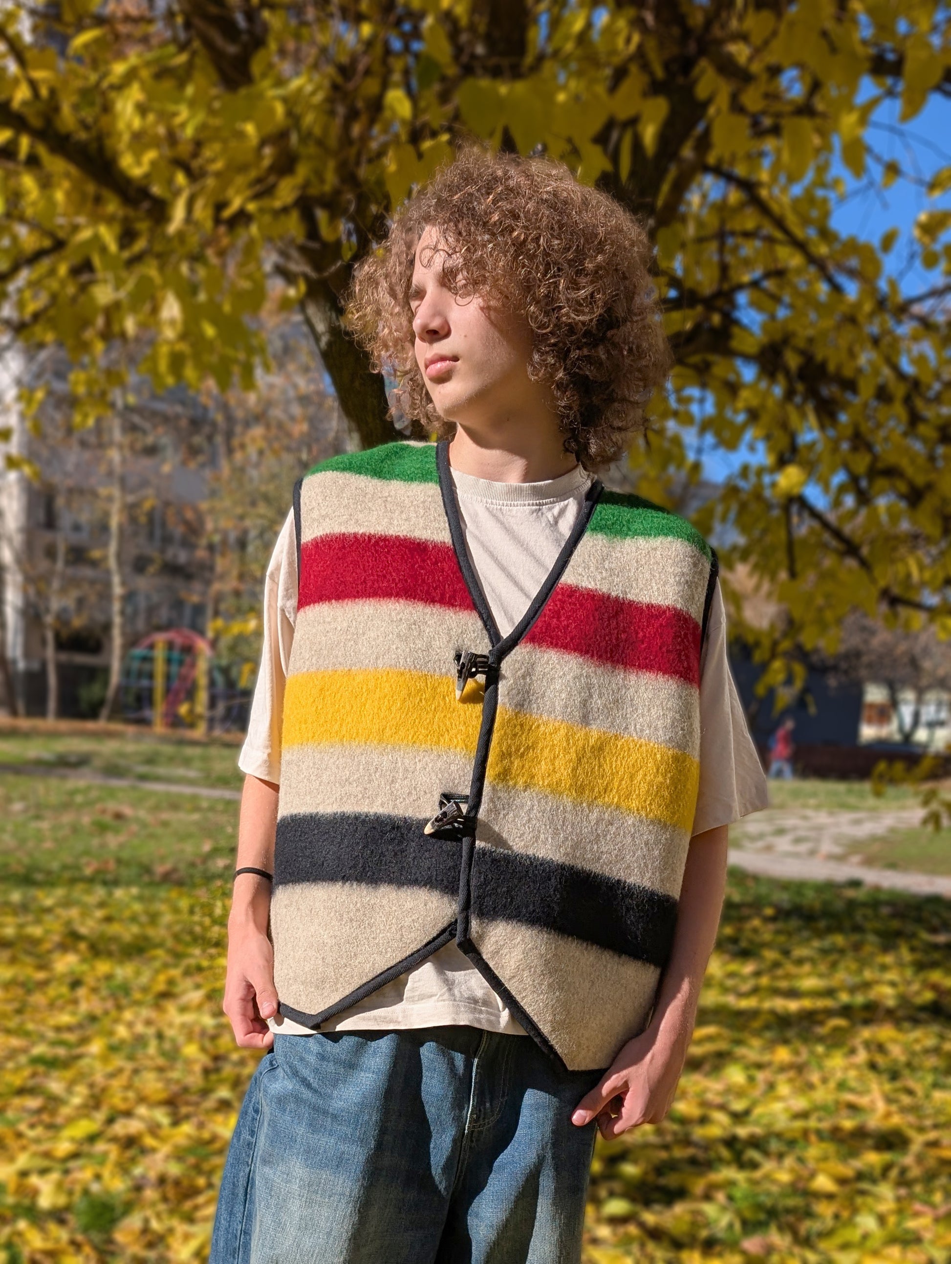 Young person wearing a colorful striped vest outdoors, upcycled from a natural wool blanket. 